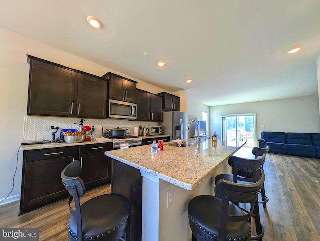 kitchen with stainless steel appliances, hardwood / wood-style floors, and a center island with sink