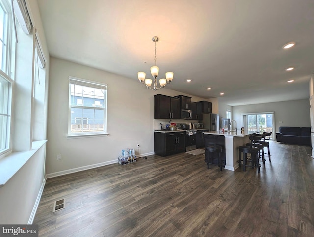 kitchen with a kitchen island with sink, stainless steel appliances, dark hardwood / wood-style floors, a kitchen bar, and decorative light fixtures