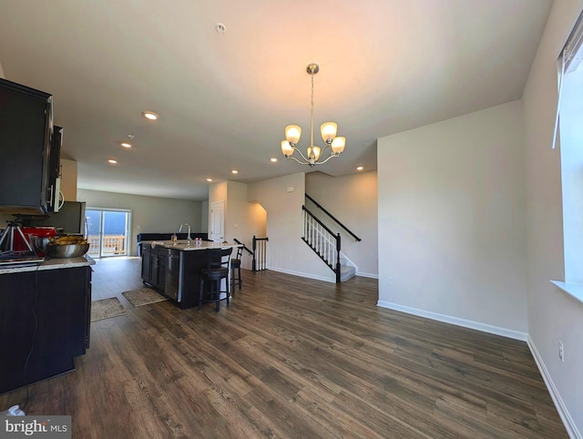 kitchen featuring dark wood-type flooring, a kitchen bar, sink, hanging light fixtures, and an island with sink