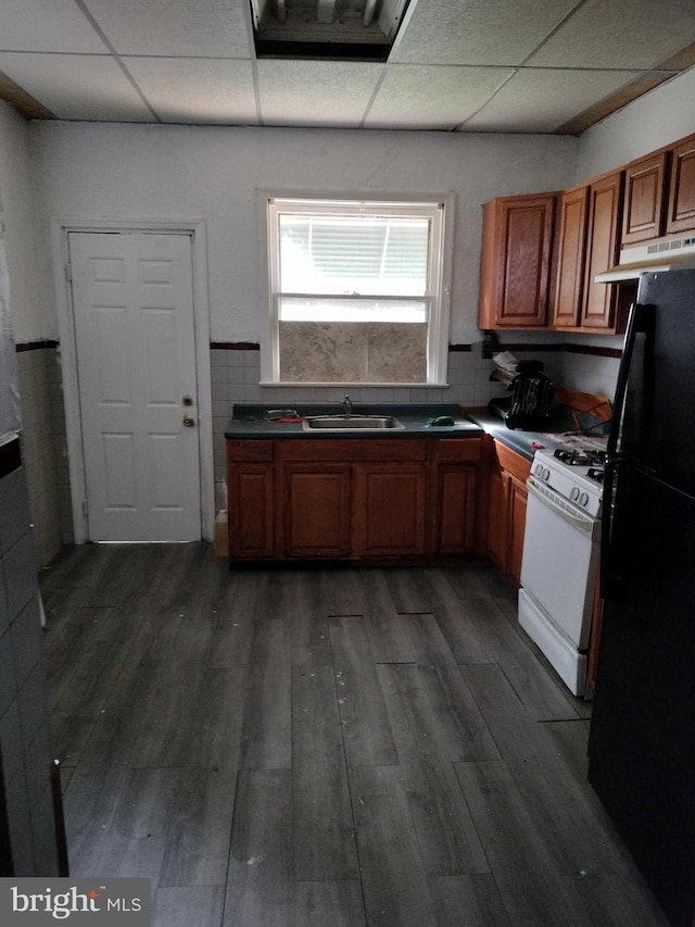 kitchen with white range with gas stovetop, a drop ceiling, black refrigerator, and dark hardwood / wood-style flooring