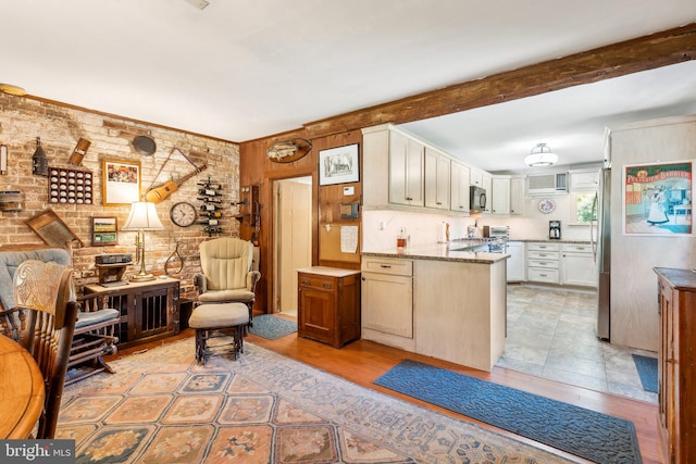 kitchen featuring beamed ceiling, brick wall, stainless steel fridge, and light stone counters