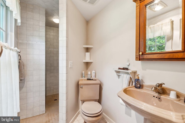 bathroom featuring a tile shower, sink, tile patterned flooring, and toilet