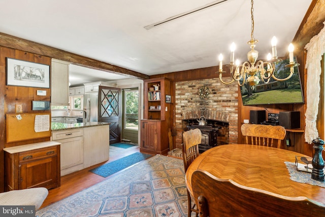 dining room with light wood-type flooring, wooden walls, a chandelier, and a wood stove