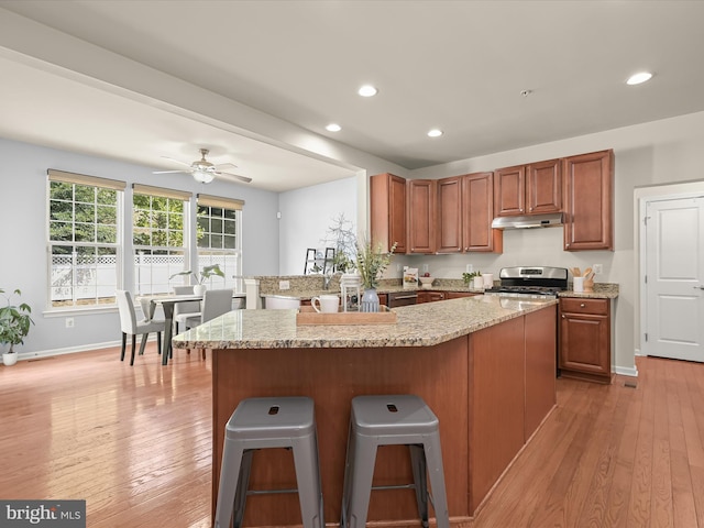 kitchen with light hardwood / wood-style floors, a kitchen breakfast bar, kitchen peninsula, and stainless steel stove