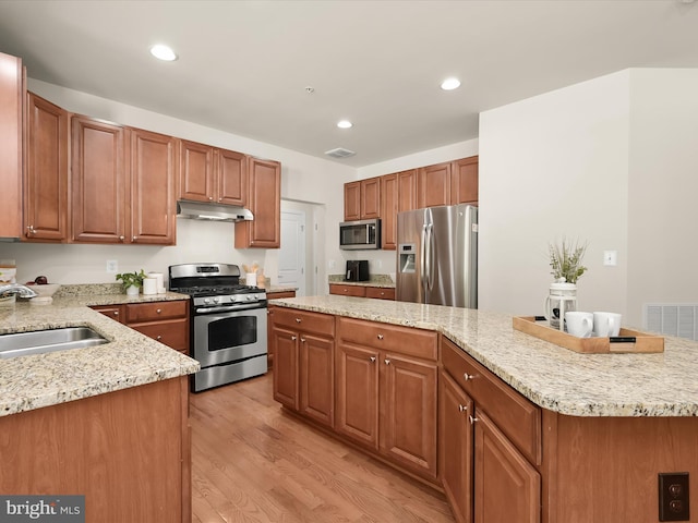 kitchen with sink, light stone counters, a kitchen island, stainless steel appliances, and light hardwood / wood-style floors