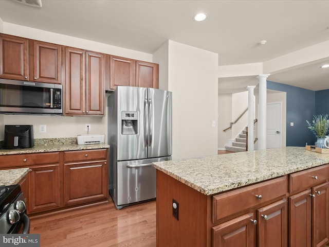 kitchen featuring decorative columns, appliances with stainless steel finishes, light stone countertops, and light hardwood / wood-style flooring