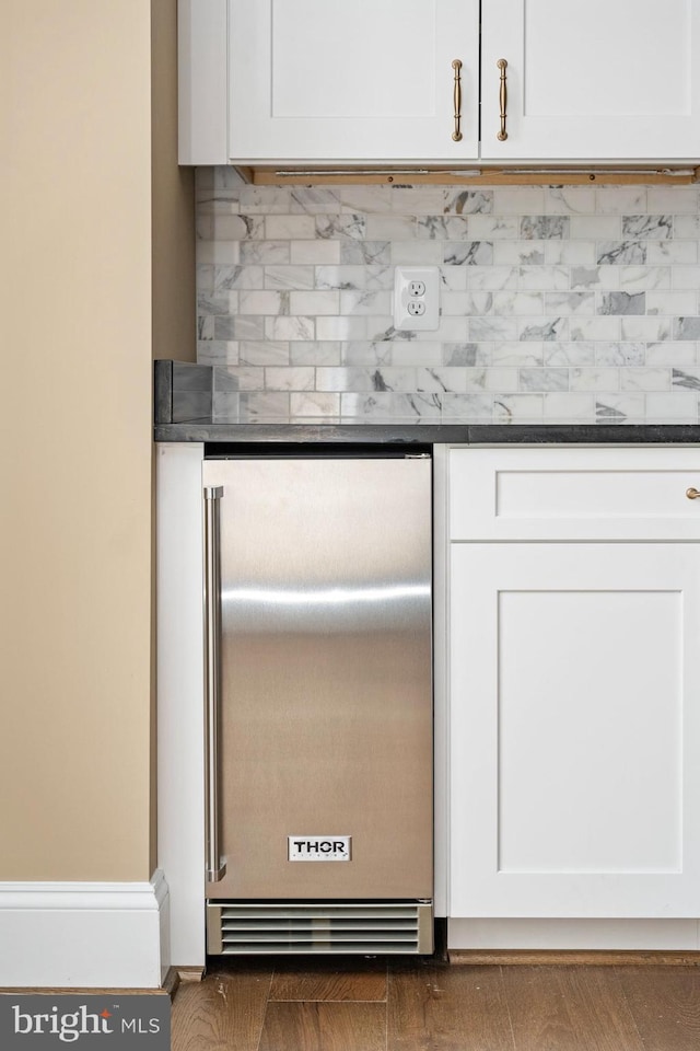 interior details featuring decorative backsplash, refrigerator, and white cabinets