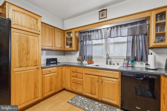 kitchen with black dishwasher, dark countertops, light wood-style flooring, glass insert cabinets, and a sink