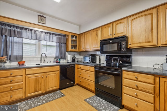 kitchen with dark countertops, black appliances, glass insert cabinets, and a sink