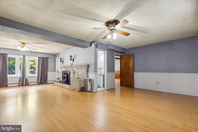 unfurnished living room with a ceiling fan, wainscoting, light wood-style flooring, and a textured ceiling