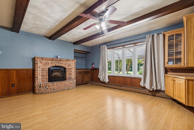 unfurnished living room featuring a wainscoted wall, light wood-style floors, baseboard heating, a brick fireplace, and beam ceiling