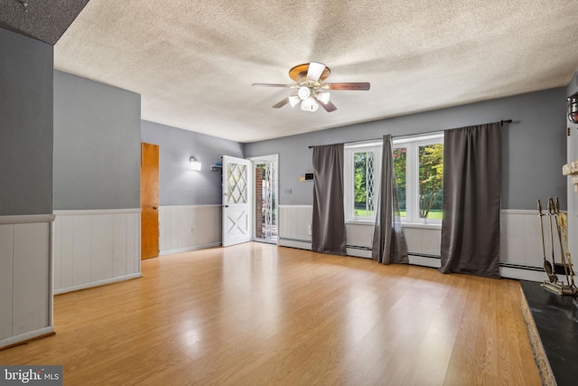 unfurnished living room with light wood finished floors, a textured ceiling, a ceiling fan, and a wainscoted wall