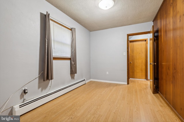 empty room with baseboards, light wood-style flooring, a baseboard heating unit, and a textured ceiling