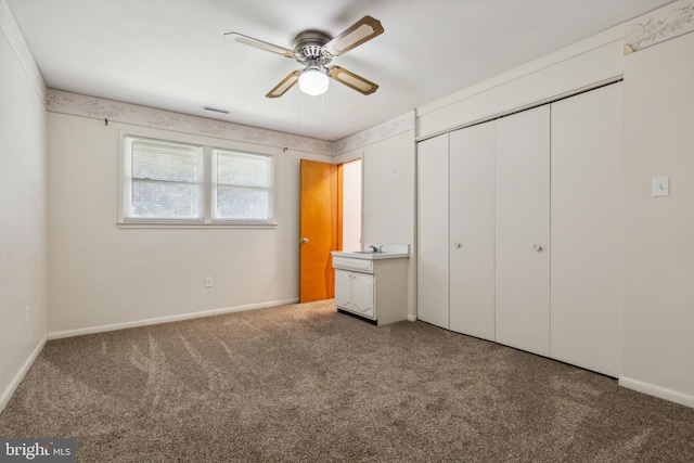 unfurnished bedroom with a closet, baseboards, ceiling fan, carpet, and a sink