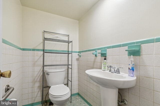 bathroom featuring wainscoting, a sink, tile walls, and toilet