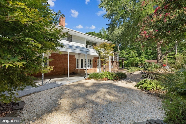 rear view of property featuring brick siding, a chimney, and a balcony