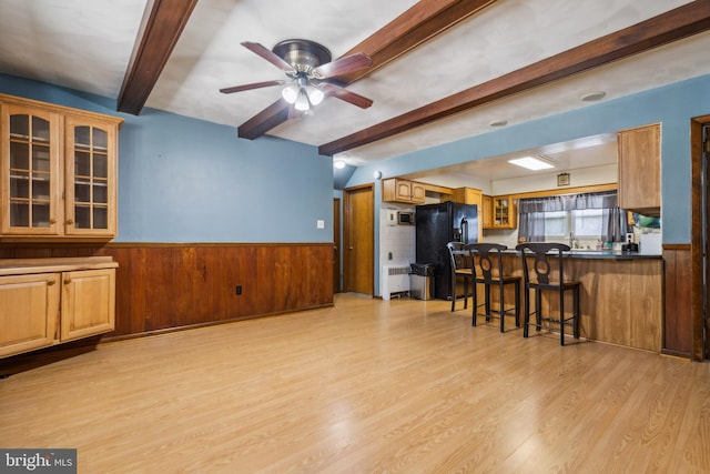 kitchen with a wainscoted wall, a peninsula, dark countertops, a kitchen bar, and glass insert cabinets