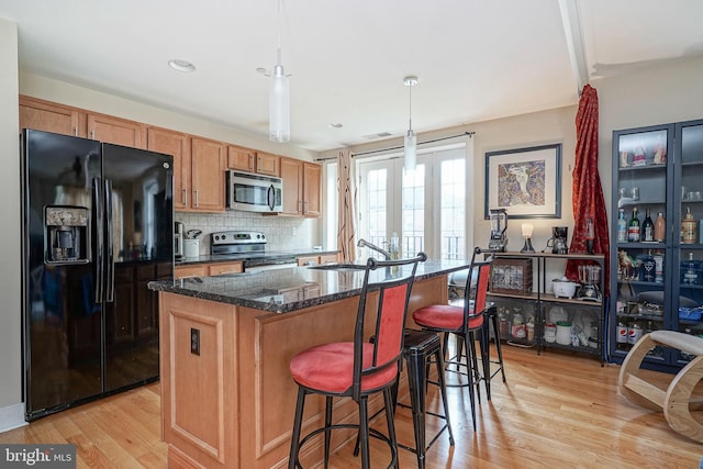 kitchen with appliances with stainless steel finishes, light wood-type flooring, pendant lighting, and a center island with sink