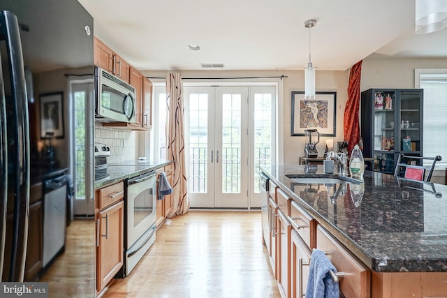 kitchen featuring a kitchen island with sink, hanging light fixtures, light wood-type flooring, stainless steel appliances, and sink