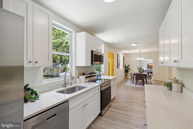 kitchen with a notable chandelier, white cabinetry, stainless steel appliances, sink, and light hardwood / wood-style flooring