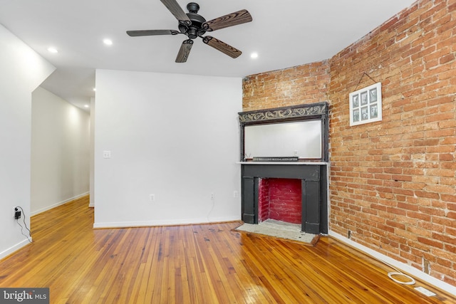 unfurnished living room featuring hardwood / wood-style floors, ceiling fan, and brick wall