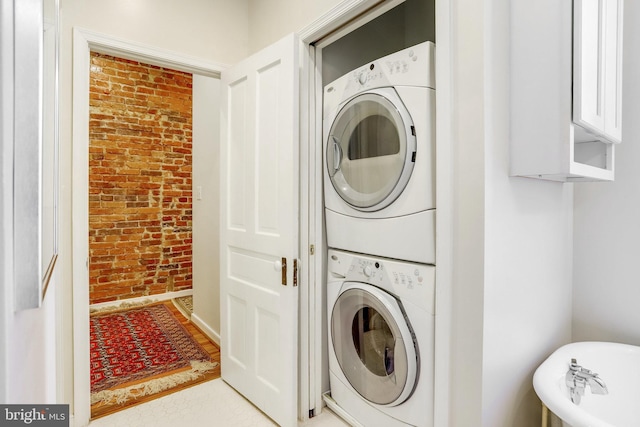 washroom featuring brick wall and stacked washer / drying machine