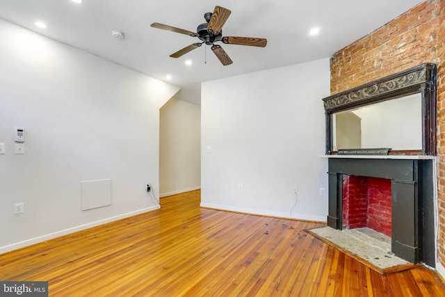 unfurnished living room featuring wood-type flooring, a brick fireplace, brick wall, and ceiling fan