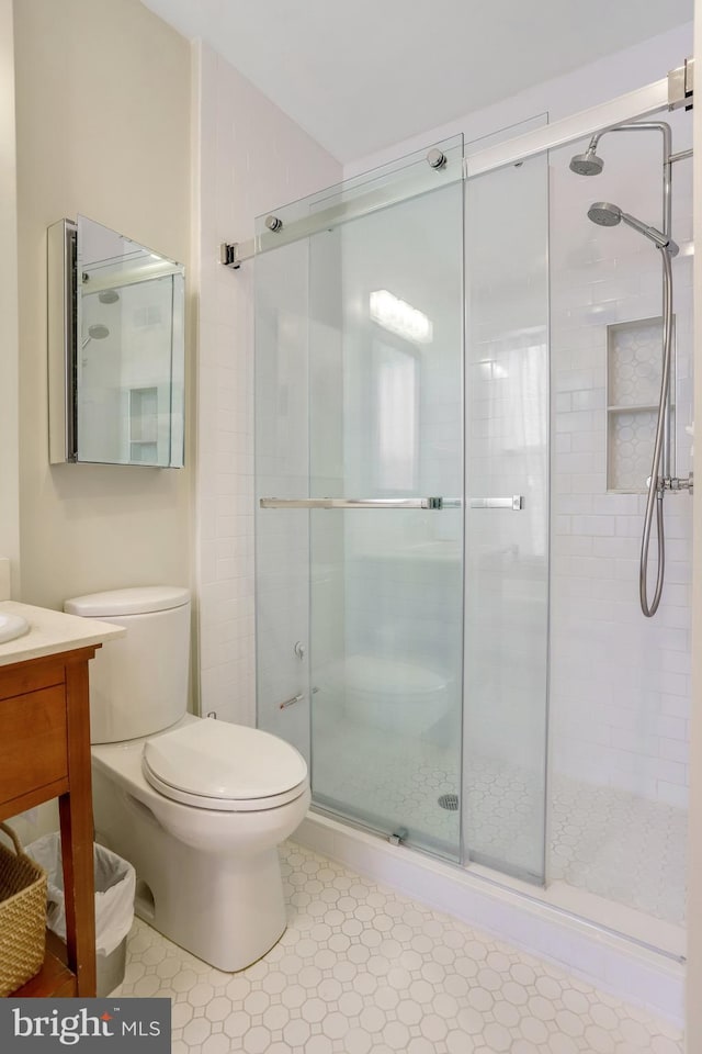 bathroom with a shower with door, vanity, tile patterned floors, and toilet