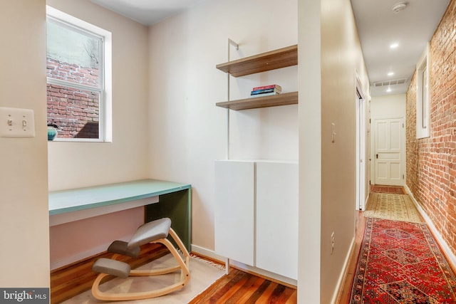 home office featuring brick wall, hardwood / wood-style flooring, and built in desk