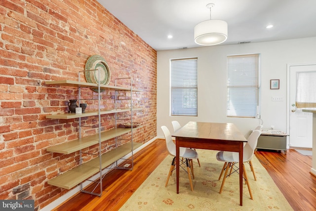 dining space with brick wall and hardwood / wood-style floors