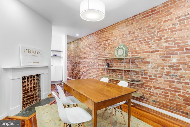 dining area with brick wall and wood-type flooring