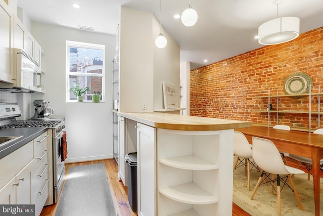 kitchen with butcher block countertops, light hardwood / wood-style floors, decorative light fixtures, stainless steel gas range, and brick wall