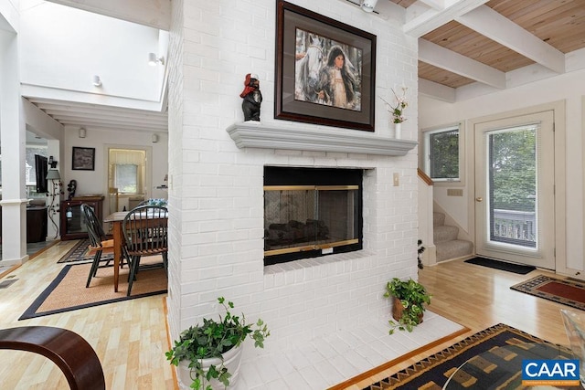 living room featuring beamed ceiling, a brick fireplace, light hardwood / wood-style flooring, and wooden ceiling