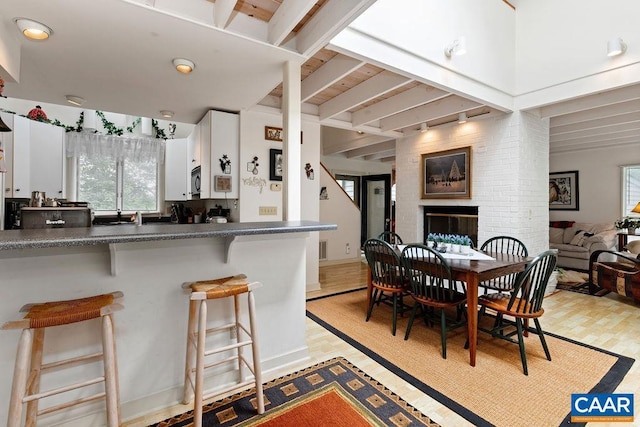 kitchen featuring a breakfast bar, a fireplace, light hardwood / wood-style floors, white cabinets, and beamed ceiling