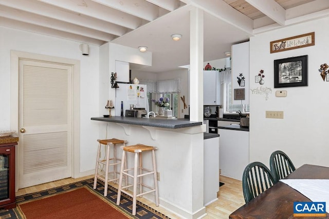 kitchen featuring a breakfast bar area, beam ceiling, white fridge, kitchen peninsula, and light wood-type flooring