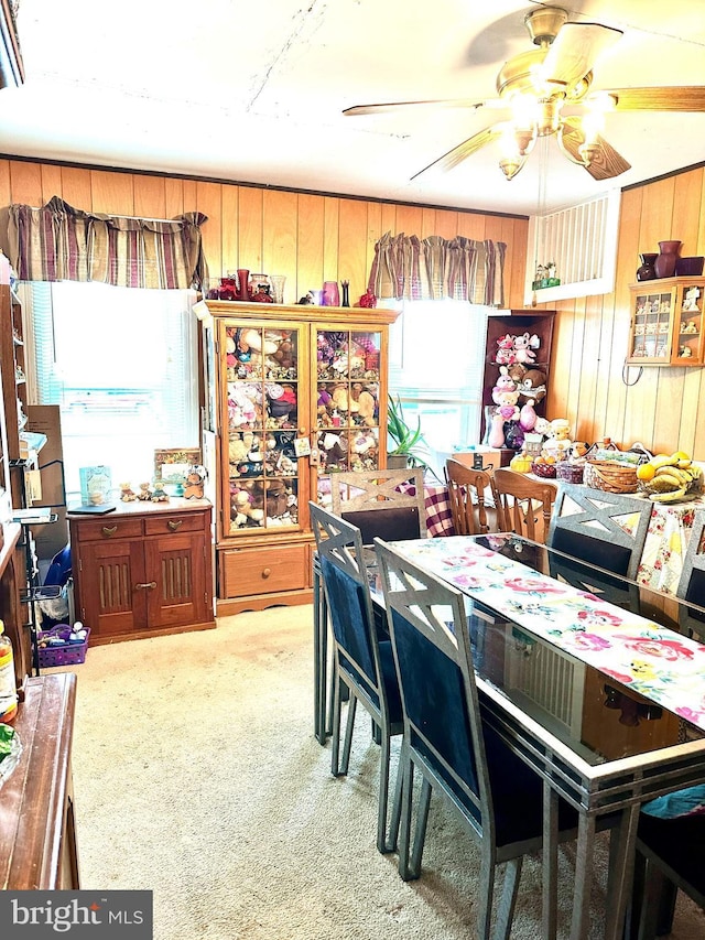 dining space featuring ceiling fan, light carpet, and wood walls