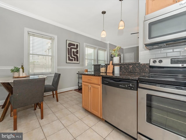 kitchen with crown molding, light tile patterned floors, dark stone counters, appliances with stainless steel finishes, and decorative light fixtures