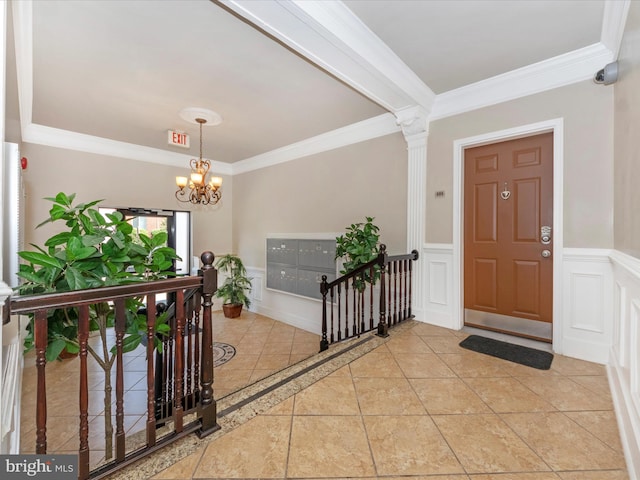 tiled foyer entrance featuring crown molding, a chandelier, and ornate columns