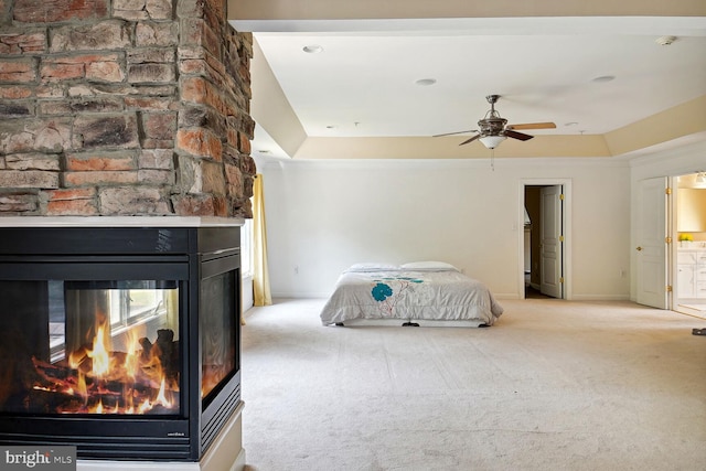 carpeted bedroom with a raised ceiling, a multi sided fireplace, and connected bathroom