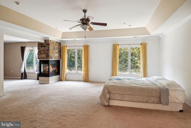 carpeted bedroom with a multi sided fireplace, ceiling fan, crown molding, and a tray ceiling