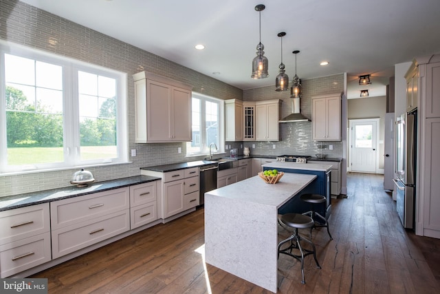 kitchen with wall chimney exhaust hood, a center island, a kitchen breakfast bar, pendant lighting, and stainless steel appliances