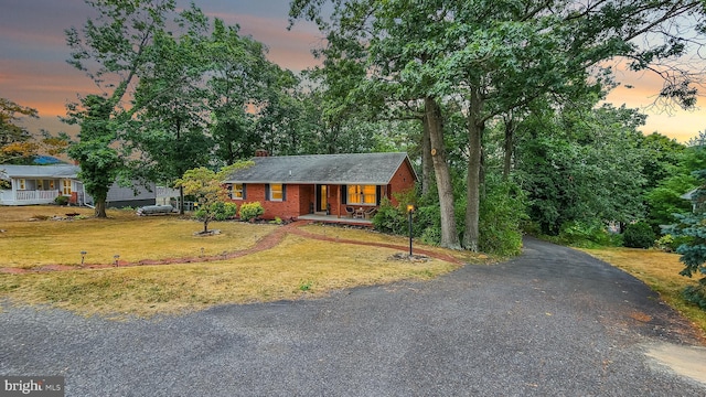 ranch-style home featuring a chimney, aphalt driveway, covered porch, a front yard, and brick siding