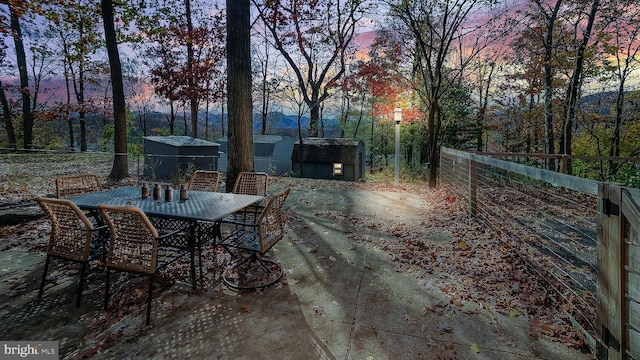 patio terrace at dusk with an outbuilding, fence, outdoor dining space, and a storage unit