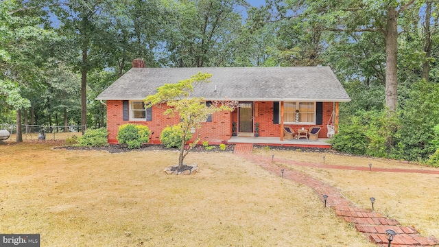 single story home with a chimney, covered porch, fence, a front lawn, and brick siding