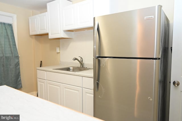 kitchen with white cabinetry, stainless steel fridge, sink, and decorative backsplash