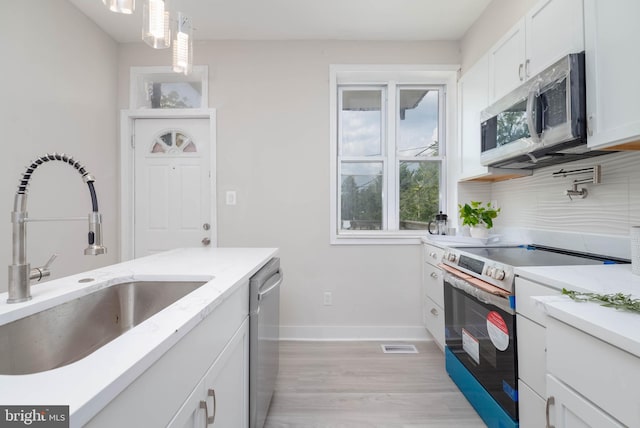 kitchen with appliances with stainless steel finishes, sink, white cabinets, hanging light fixtures, and light hardwood / wood-style flooring