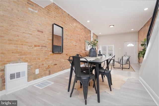 dining space featuring brick wall and light hardwood / wood-style floors