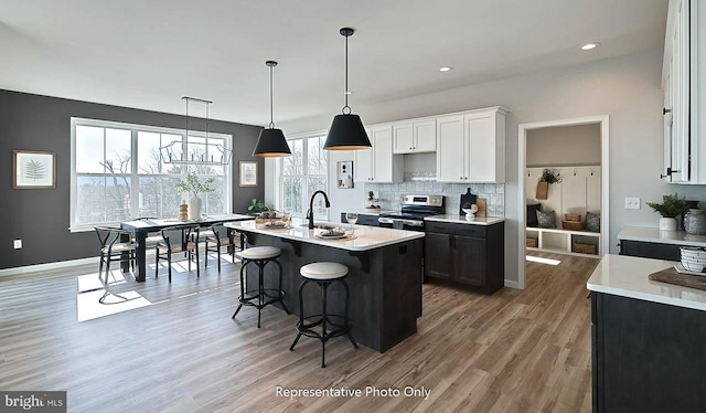 kitchen with hardwood / wood-style flooring, decorative backsplash, an island with sink, stainless steel electric range, and white cabinets