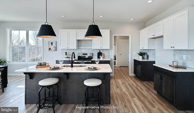 kitchen with light hardwood / wood-style floors, white cabinets, tasteful backsplash, pendant lighting, and a center island with sink