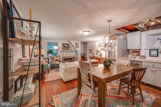 dining area featuring a tiled fireplace, light hardwood / wood-style flooring, and an inviting chandelier